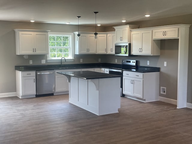 kitchen with dark hardwood / wood-style floors, a kitchen island, appliances with stainless steel finishes, decorative light fixtures, and white cabinetry