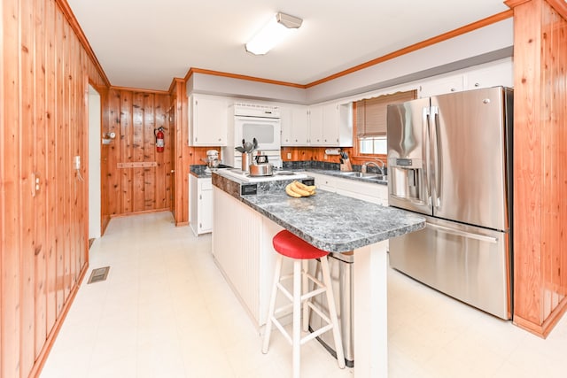 kitchen featuring light tile flooring, stainless steel fridge, a kitchen bar, white cabinetry, and oven