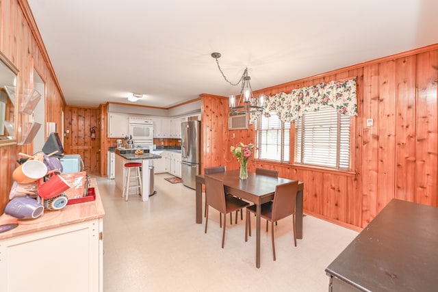 dining space with light tile floors, a notable chandelier, wooden walls, and ornamental molding