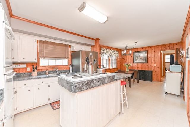 kitchen with a chandelier, a kitchen island, wooden walls, stainless steel fridge with ice dispenser, and white cabinets