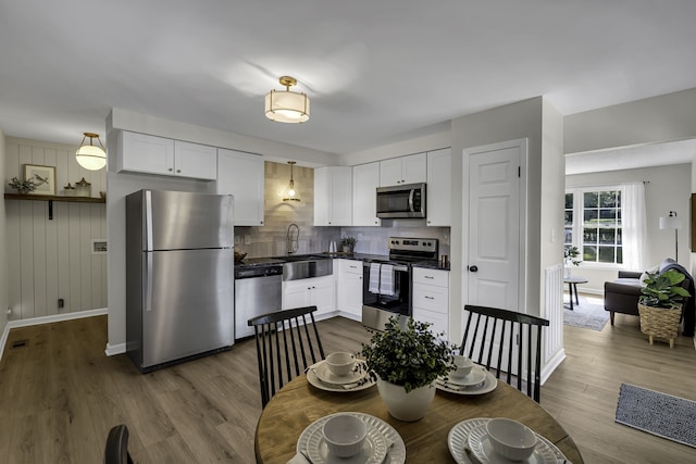 kitchen with pendant lighting, hardwood / wood-style floors, appliances with stainless steel finishes, and white cabinetry