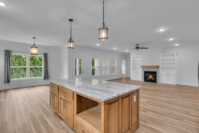 kitchen with a stone fireplace, a kitchen island, light hardwood / wood-style flooring, ceiling fan, and hanging light fixtures