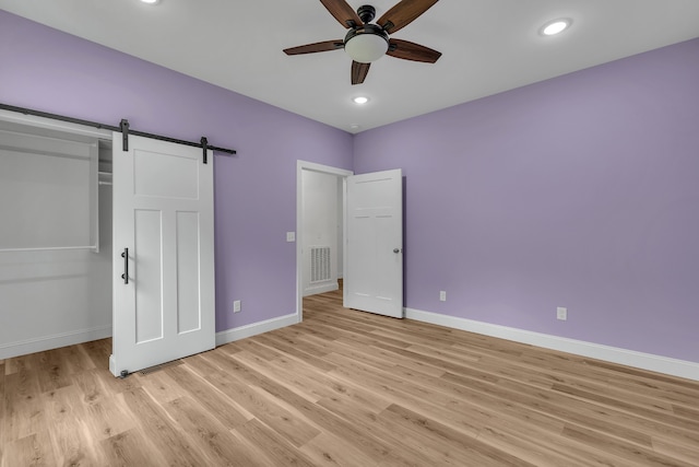 unfurnished bedroom featuring a barn door, a closet, ceiling fan, and light wood-type flooring