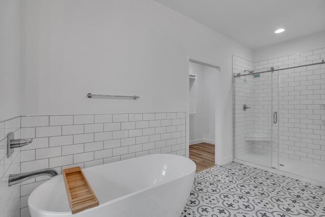 bathroom with tile walls, shower with separate bathtub, and tile floors