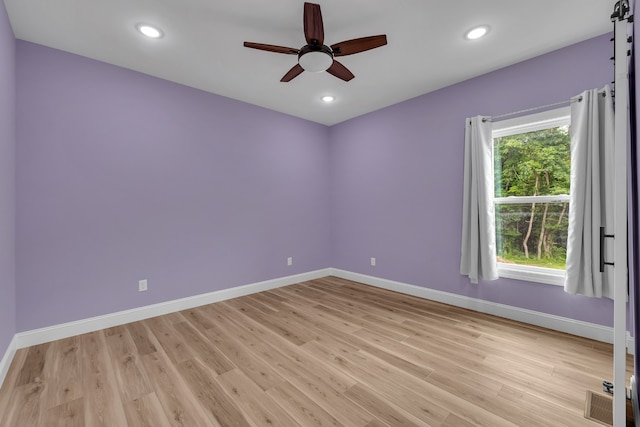 spare room with a barn door, light hardwood / wood-style floors, ceiling fan, and a wealth of natural light