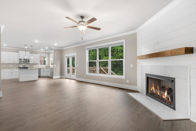 unfurnished living room with ceiling fan, a premium fireplace, dark wood-type flooring, crown molding, and sink