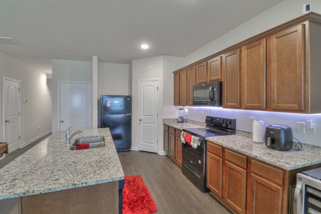 kitchen with light stone countertops, black appliances, dark hardwood / wood-style flooring, a kitchen island with sink, and sink