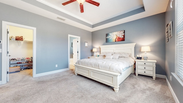 carpeted bedroom with crown molding, a closet, ceiling fan, a walk in closet, and a raised ceiling