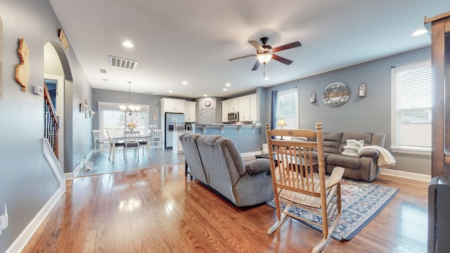 living room featuring light hardwood / wood-style flooring, ceiling fan with notable chandelier, and a wealth of natural light