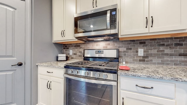 kitchen with appliances with stainless steel finishes, white cabinetry, tasteful backsplash, and light stone counters