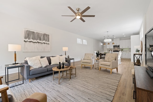 living room featuring light wood-type flooring and ceiling fan with notable chandelier