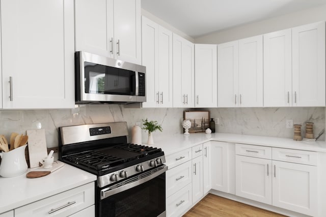 kitchen with backsplash, stainless steel appliances, light wood-type flooring, and white cabinetry