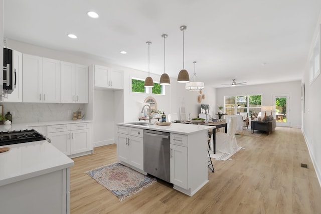 kitchen with decorative light fixtures, a kitchen island with sink, light hardwood / wood-style floors, white cabinets, and dishwasher