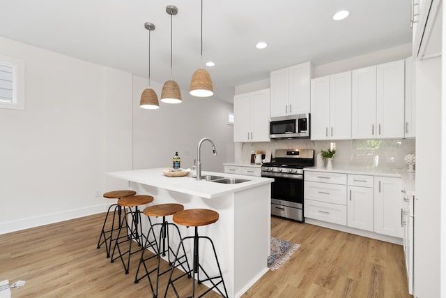 kitchen with decorative light fixtures, appliances with stainless steel finishes, light hardwood / wood-style floors, sink, and white cabinets