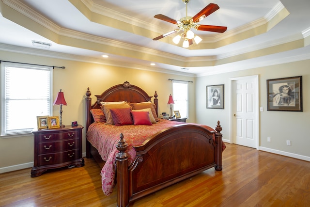 bedroom with a tray ceiling, ceiling fan, wood-type flooring, and crown molding