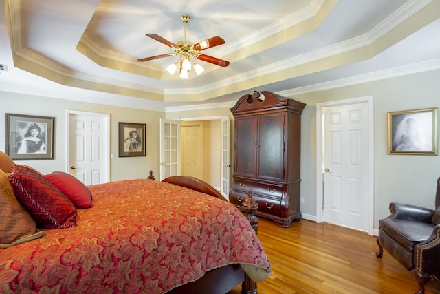 bedroom with a tray ceiling, ceiling fan, light wood-type flooring, and crown molding