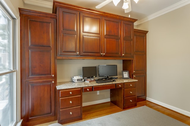 unfurnished office featuring built in desk, ceiling fan, light hardwood / wood-style floors, and crown molding