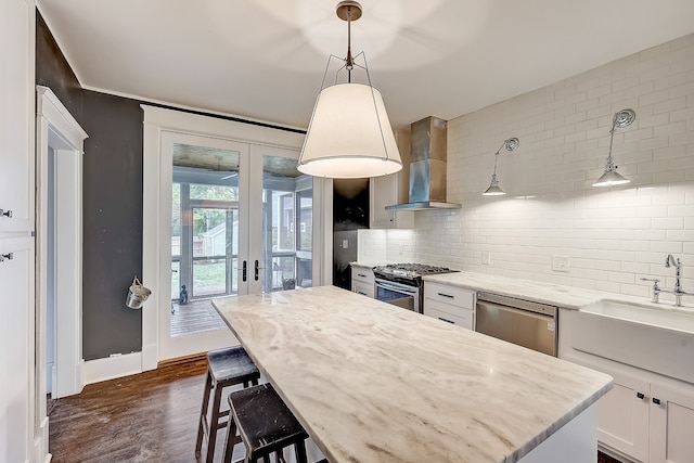 kitchen with stainless steel dishwasher, backsplash, gas range, wall chimney exhaust hood, and white cabinetry