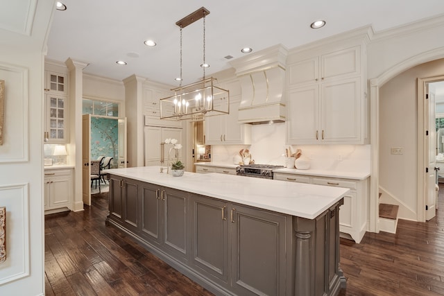 kitchen with custom range hood, decorative light fixtures, white cabinets, and a center island