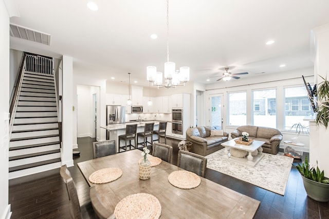 dining space with ceiling fan with notable chandelier and dark hardwood / wood-style flooring