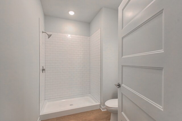 bathroom with toilet, a tile shower, and hardwood / wood-style flooring