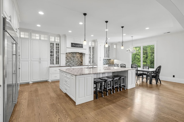 3609 Leipers Valley Trl, Franklin, TN 37064 - kitchen featuring light stone countertops, white cabinetry, light wood-type flooring, an island with sink, and tasteful backsplash