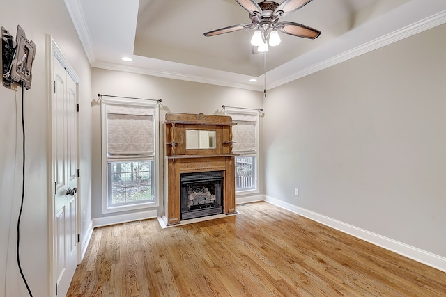 unfurnished living room with crown molding, a tray ceiling, ceiling fan, and light wood-type flooring