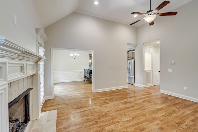 unfurnished living room featuring high vaulted ceiling, ceiling fan with notable chandelier, a fireplace, and light wood-type flooring