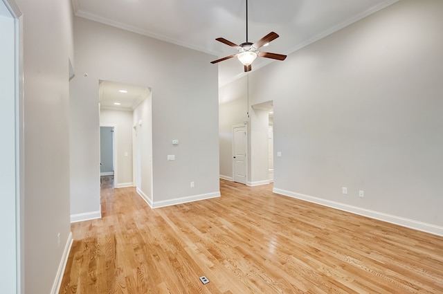 spare room with crown molding, ceiling fan, a towering ceiling, and light wood-type flooring