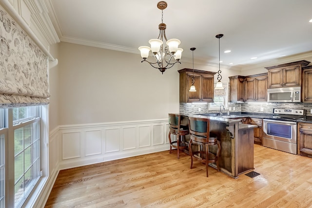 kitchen with hanging light fixtures, appliances with stainless steel finishes, a chandelier, light hardwood / wood-style floors, and tasteful backsplash