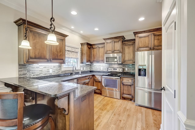 kitchen featuring appliances with stainless steel finishes, backsplash, a kitchen bar, decorative light fixtures, and light hardwood / wood-style flooring