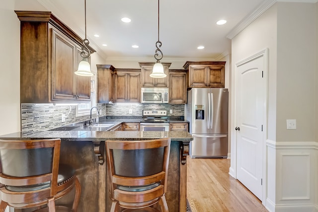 kitchen with appliances with stainless steel finishes, a breakfast bar, light hardwood / wood-style floors, tasteful backsplash, and decorative light fixtures