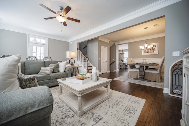 living room with dark wood-type flooring, a fireplace, ceiling fan with notable chandelier, and ornamental molding