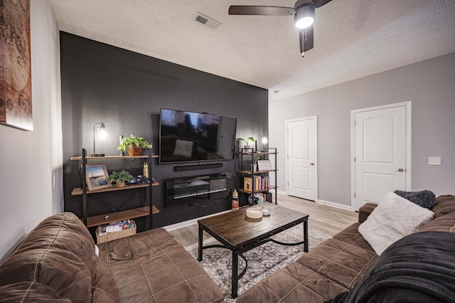 living room featuring ceiling fan, light hardwood / wood-style floors, and a textured ceiling