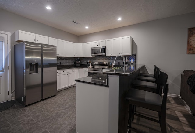 kitchen with kitchen peninsula, appliances with stainless steel finishes, a breakfast bar area, tasteful backsplash, and white cabinetry