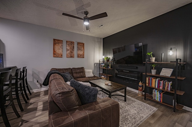 living room featuring dark hardwood / wood-style flooring, ceiling fan, and a textured ceiling