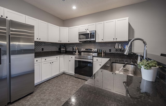 kitchen with appliances with stainless steel finishes, tasteful backsplash, white cabinets, dark tile floors, and sink