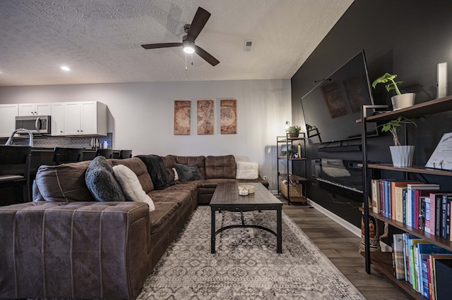 living room with dark hardwood / wood-style floors, ceiling fan, and a textured ceiling