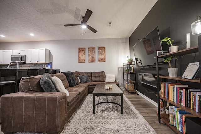 living room with ceiling fan, dark wood-type flooring, and a textured ceiling