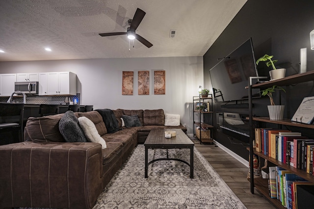 living room with ceiling fan, a textured ceiling, and dark wood-type flooring