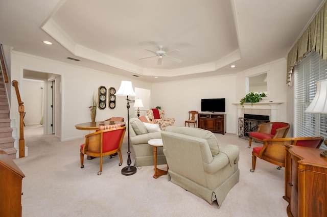 living room with light carpet, a fireplace, ceiling fan, and a tray ceiling