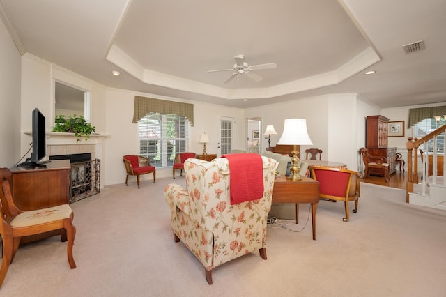 living room with ceiling fan, a tile fireplace, light carpet, and a raised ceiling