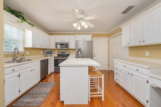 kitchen with ceiling fan, appliances with stainless steel finishes, light hardwood / wood-style floors, sink, and a center island