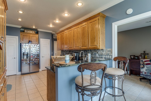 kitchen featuring light tile floors, dark stone counters, a breakfast bar, backsplash, and stainless steel refrigerator with ice dispenser