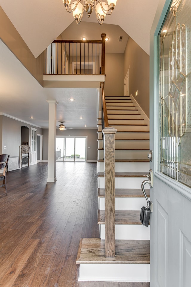 stairs with dark hardwood / wood-style flooring, a high ceiling, ornate columns, and ceiling fan with notable chandelier