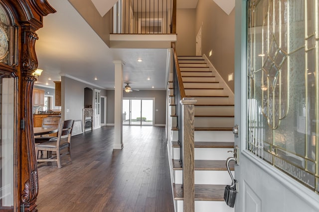 foyer entrance with ceiling fan, dark wood-type flooring, ornamental molding, and ornate columns