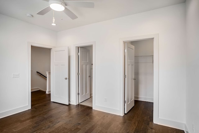 unfurnished bedroom featuring a closet, a walk in closet, ceiling fan, and dark hardwood / wood-style flooring