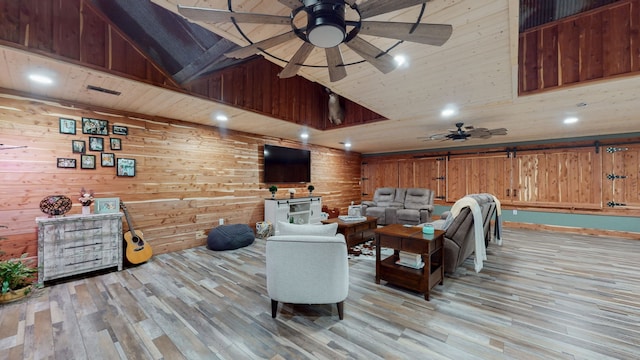 living room with ceiling fan, light hardwood / wood-style flooring, wooden walls, and a towering ceiling