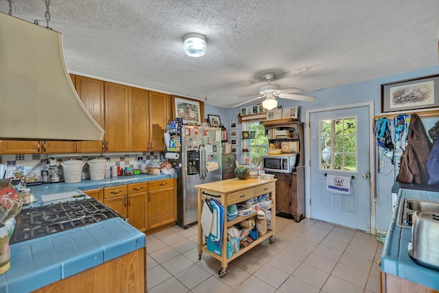 kitchen with custom range hood, light tile patterned floors, a textured ceiling, ceiling fan, and stainless steel appliances