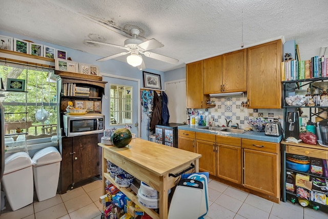 kitchen featuring ceiling fan, sink, a textured ceiling, light tile patterned floors, and backsplash